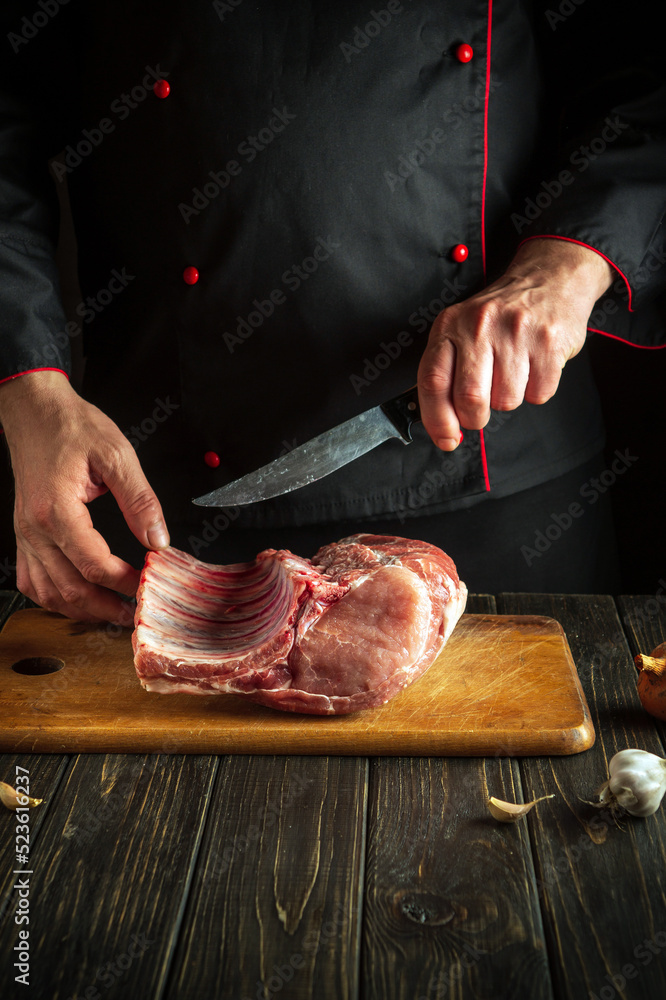 Butcher cuts raw ribs on a cutting board before barbecuing. Cooking delicious food in the hotel kitchen.