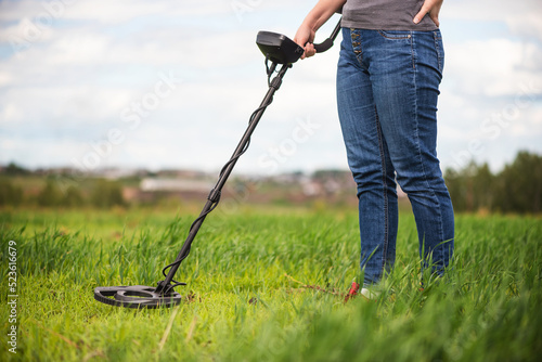 Foto Girl with metal detector walks on the green field