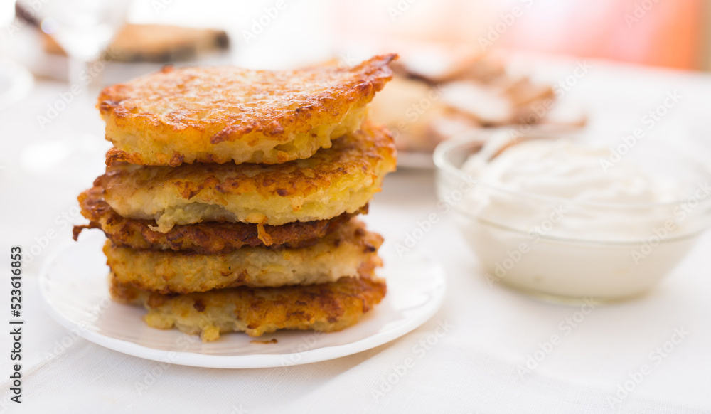 Fried grated potato pancakes with sour cream on white plate Fried grated potato pancakes with sour cream on white plate