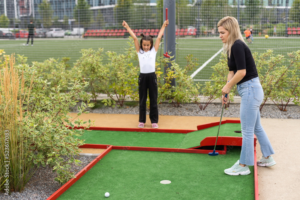 Naklejka premium little girl and mother playing mini golf