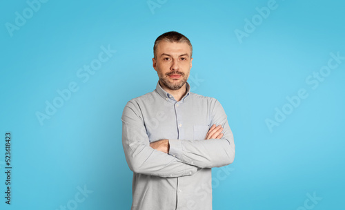 Serious Middle Aged Businessman Crossing Hands Posing Over Blue Background