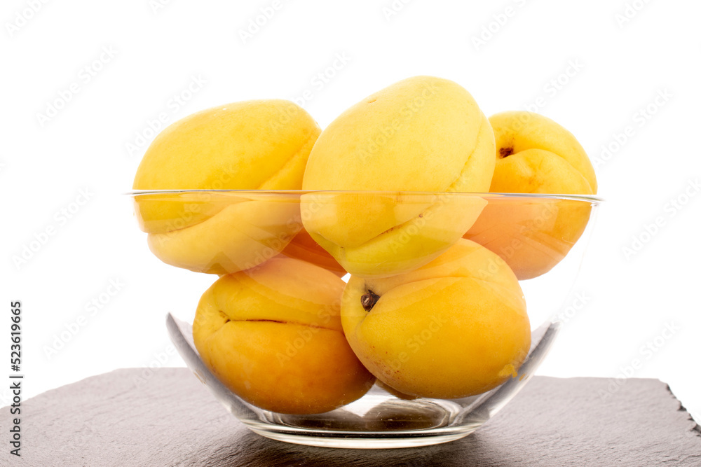 Several bright yellow juicy pineapple apricots in a glass bowl, macro isolated on a white background.