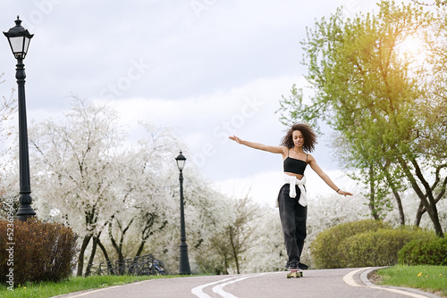 Young african american woman riding on the skateboard on the road in the park