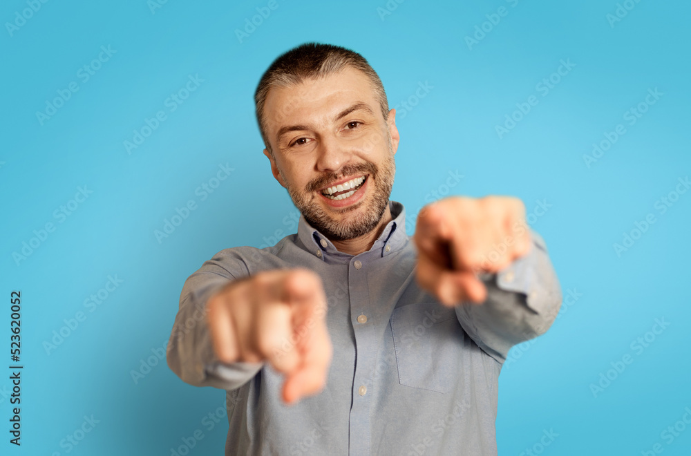 Cheerful Middle Aged Man Pointing Fingers At Camera, Blue Background