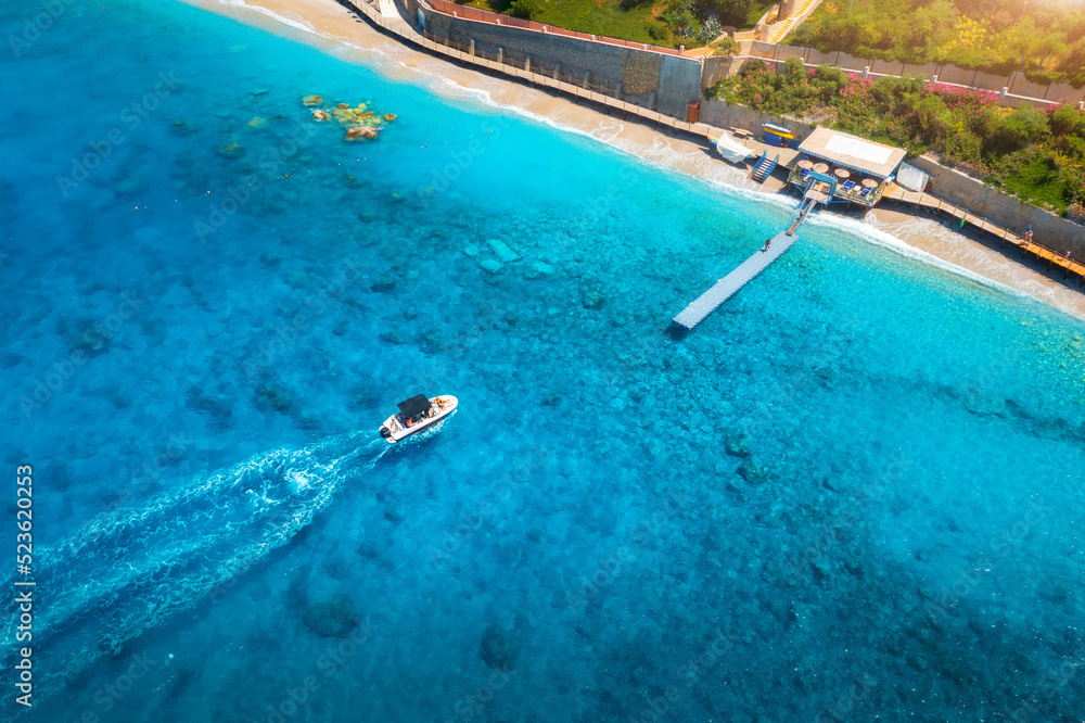 Aerial view of speed boat on blue sea at sunset in summer. Motorboat in Blue Lagoon, sandy beach, trees, clear azure water. Tropical landscape with yacht, green forest. Top view. Oludeniz, Turkey
