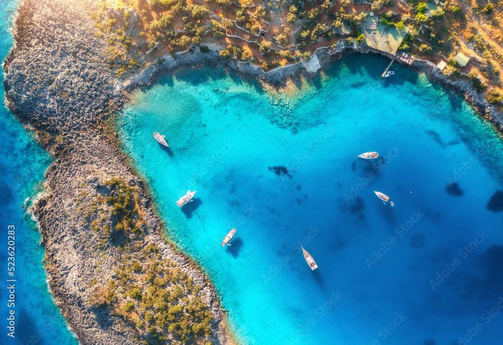 Aerial view of beautiful yachts and boats on the sea at sunset in summer. Akvaryum koyu in Turkey. Top view of luxury yachts, sailboats, clear blue water, rock, lagoon, mountain, green trees. Travel