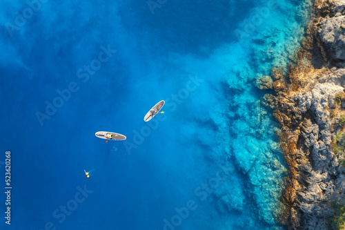 Aerial view of people on floating sup boards on blue sea, rocks, stones at sunset in summer in Oludeniz, Turkey. Tropical landscape. Kayaks on clear water. Active travel. Top view of canoe. Sport