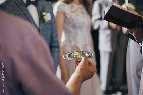 Priest holding plate with stylish wedding rings in church for holy matrimony. Wedding ceremony in cathedral. Wedding rings for bride and groom
