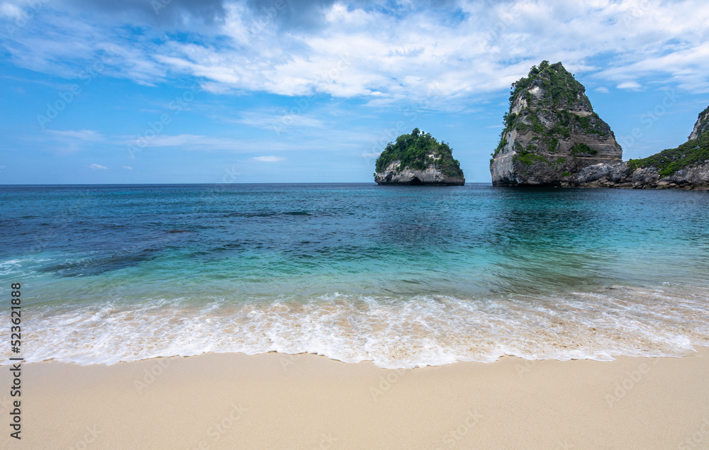 Scenery of sunny day with sand beach, turquoise ocean, blue sky, waves and mountains. View of Diamond beach, Nusa Penida, Bali island, Indonesia. Wallpaper background. Natural scenery.