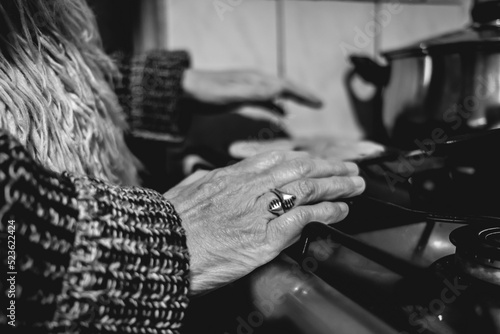 Beautiful hands of elderly latino woman cooking on traditional kitchen stove with gas burners with traditional toaster with 'sopaipillas' (fried pastry) and pots (in black and white) © Samuel Ponce