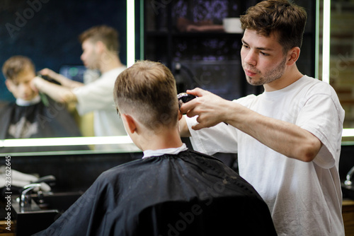 Young barber doing haircut in the barbershop. Hairdresser job background