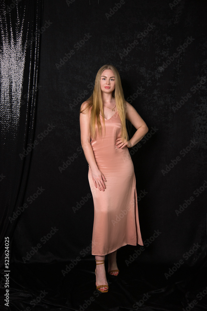 beautiful blond woman with long hair in a pink dress sitting on a chair on black background beautiful blond woman with long hair in a pink dress sitting on a chair on black background