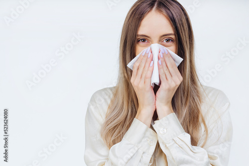 Young sick girl in white shirt sneeze holding tissue handkerchief and blowing wiping her running nose. Student girl has seasonal allergy or chronic sinusitis disease concept