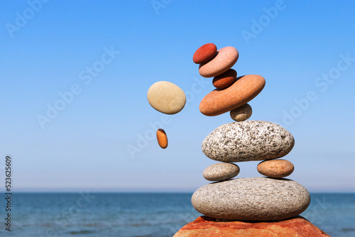 The fall of the pyramid of balanced stones on blue sky background. The concept of fall risk and unstable equilibrium. photo