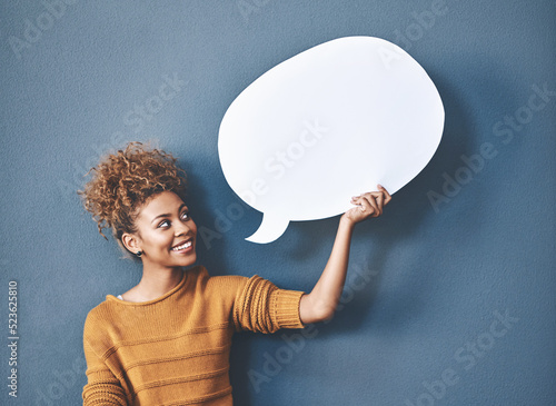 Young woman holding a speech bubble against a grey background in a studio. Portrait of a casual, happy and smiling female holding copy space empty shape for social media, chat and voice or message. photo