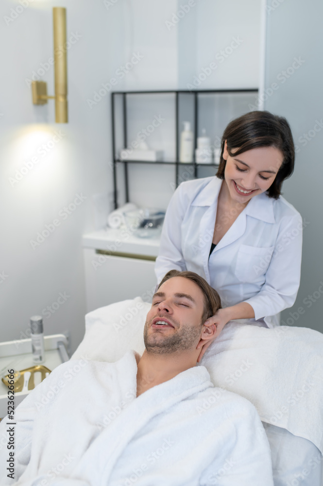 Dark-haired professional doing face massage to a male customer Dark-haired professional doing face massage to a male customer