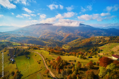 Aerial view of mountains at sunrise in autumn in Ukraine. Colorful landscape with mountain road, forest, houses on the hills, sunlight, sky in fall.