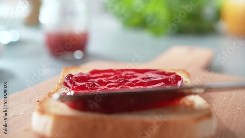 Spreading Red Jam on a Slightly Browned Toast with Table Knife on Cutting Board in Slow Motion