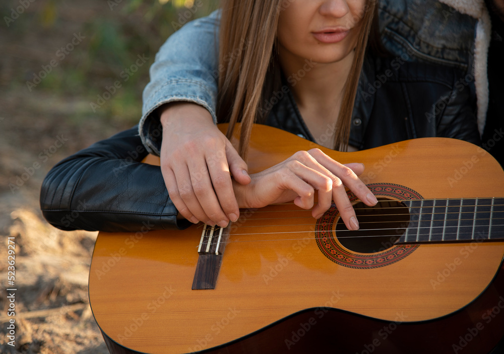 Fototapeta premium romantic couple sitting on the beach in autumn forest near lake and playing guitar. Hands closeup