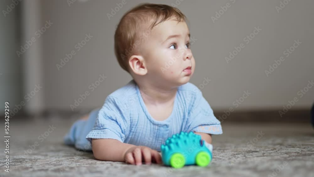 Beautiful baby lying on belly on the floor with toy in front of him. Cute child looks up and smiles to somebody adorably. Blurred backdrop. Beautiful baby lying on belly on the floor with toy in front of him. Cute child looks up and smiles to somebody adorably. Blurred backdrop.
