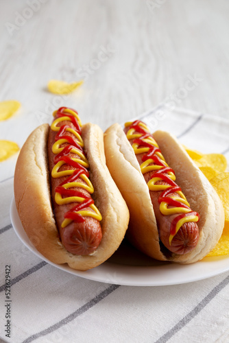 Homemade Hot Dog with Ketchup and Yellow Mustard with Chips on a Plate, side view. Close-up. photo