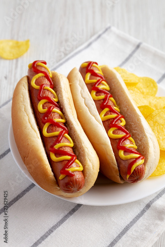 Homemade Hot Dog with Ketchup and Yellow Mustard with Chips on a Plate, low angle view.
