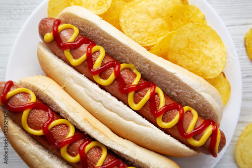 Homemade Hot Dog with Ketchup and Yellow Mustard with Chips on a Plate, top view. Flat lay, overhead, from above. Close-up.