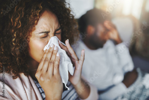 Ill or sick woman with allergy, sinus infection sneezing in tissue or blowing nose during flu season at home. Sick girl caught a bad cold showing symptoms of covid, or suffering from a virus disease photo