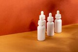 Set of white cosmetic bottles with a dropper on a beige background with hard shadows. The concept of face and body care at home and in a beauty salon
