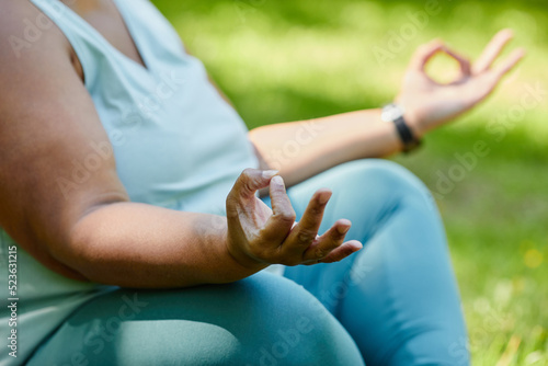 Close up of overweight black woman doing yoga outdoors and meditating with focus on hand pose, copy space
