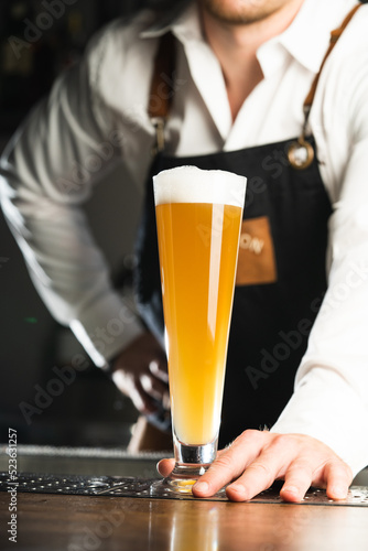 Beer. A professional bartender in the background, men in a white shirt and a black apron, the trend drinks concept. Vertical photo 