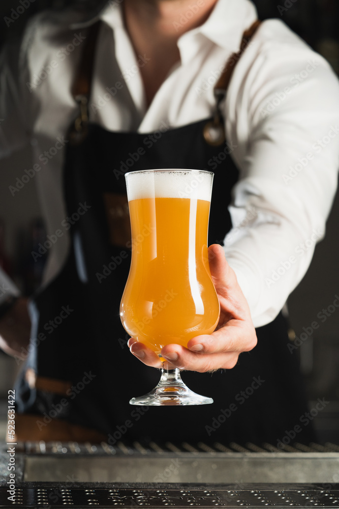 Beer. A professional bartender in a white shirt and black apron holds a glass of beer, the trend drinks concept. Vertical photo Beer. A professional bartender in a white shirt and black apron holds a glass of beer, the trend drinks concept. Vertical photo