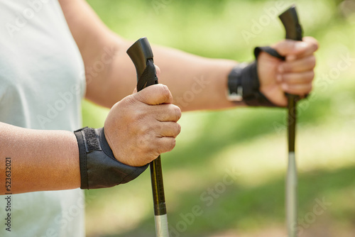 Close up of overweight woman walking outdoors with nordic poles and enjoying cardio workout, copy space