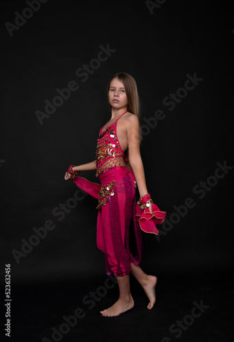a young beautiful blonde girl in a pink outfit dances an oriental belly dance on black background