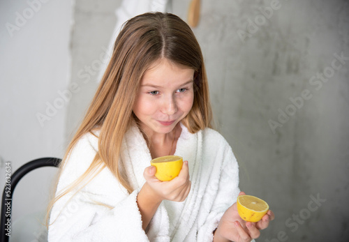 beautiful blonde girl with long hair in a white bathrobe in a bathroom with lemons takes care of herself