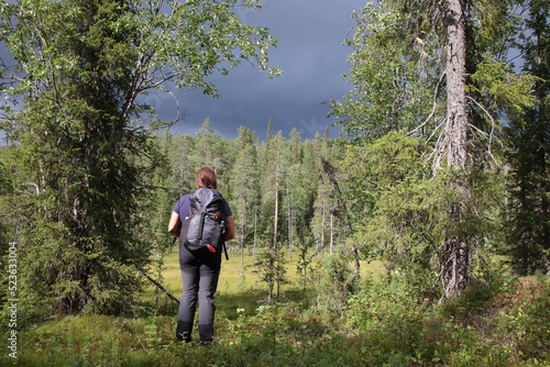 Woman with a rucksack hiking in the nature. The sun is shining, but the sky is dark. Soon it will rain.