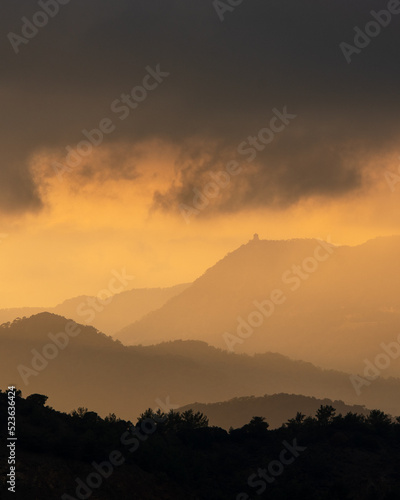 Sunset with stormy cloud sky and dramatic orange sunlight above mountain peaks