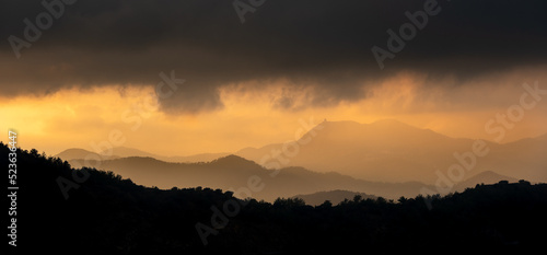 Sunset with stormy cloud sky and dramatic orange sunlight above mountain peaks