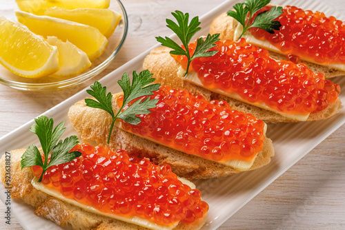 Sandwiches with red caviar on a white plate. Gourmet appetizer of trout caviar on a slice of french baguette with butter. Salted salmon roe for seafood fish delicacy concept.