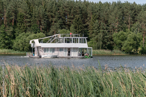 Fotografia A ship in the form of a two-story houseboat floats along the river