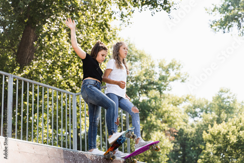 Skater children girls reade to ride on penny board on skate sport ramp at sunset together. Sports equipment for kids. Active teenager with pennyboard on skate park playground.