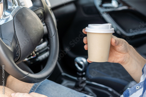 Male hands with paper cup inside a car.