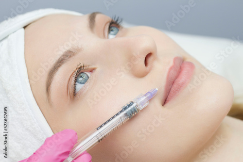 A woman with beautiful clear skin. A cosmetologist makes injections to increase the lips and anti-wrinkles of a beautiful woman. Women's cosmetology in a beauty salon.