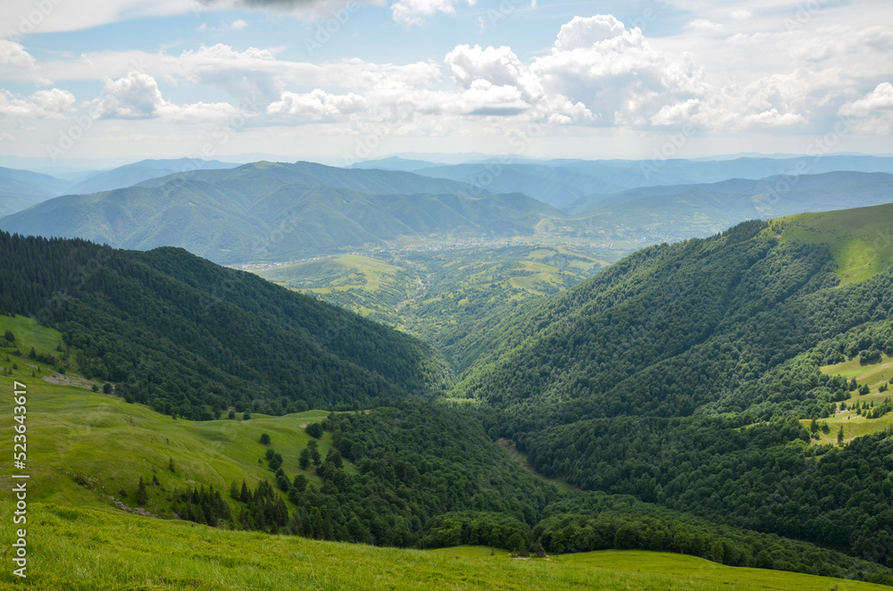 Summer nature landscape, view from the mountain range to the valley covered with forest and village from the distance. Carpathian Mountains, Ukraine