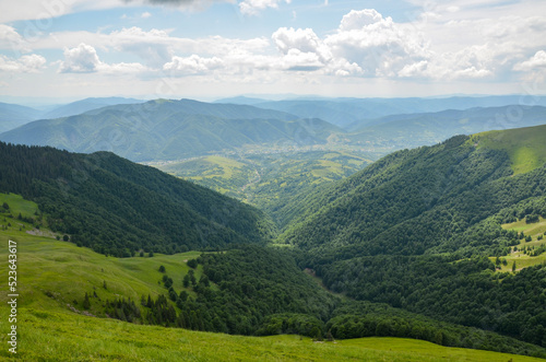 Summer nature landscape, view from the mountain range to the valley covered with forest and village from the distance. Carpathian Mountains, Ukraine