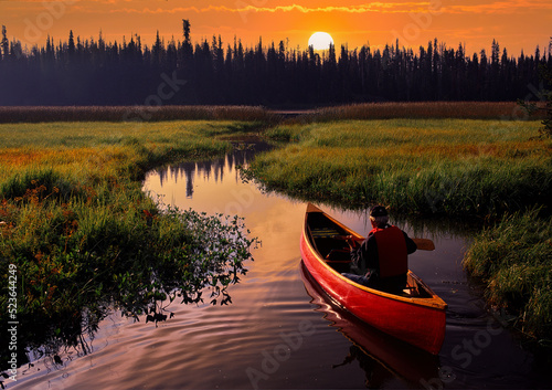 A red canoe at sunrise navigating a small stream that leads to Hosmer lake near Bend, Oregon photo