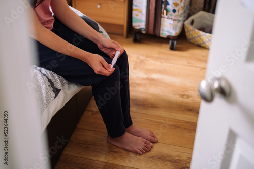 Worry Unrecognizable Woman Sitting On Bed and Holding Pregnancy Test