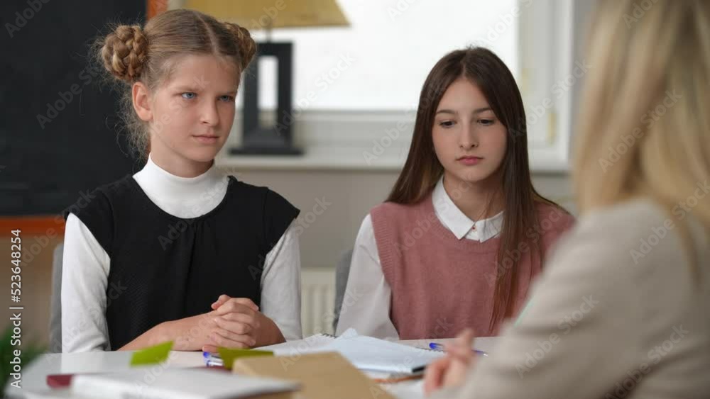 Stressed Caucasian teen schoolgirl leaving classroom as teacher scolding student. Portrait of dissatisfied cute girl walking away as classmate and tutor sitting at desk in school. Education failures Stressed Caucasian teen schoolgirl leaving classroom as teacher scolding student. Portrait of dissatisfied cute girl walking away as classmate and tutor sitting at desk in school. Education failures