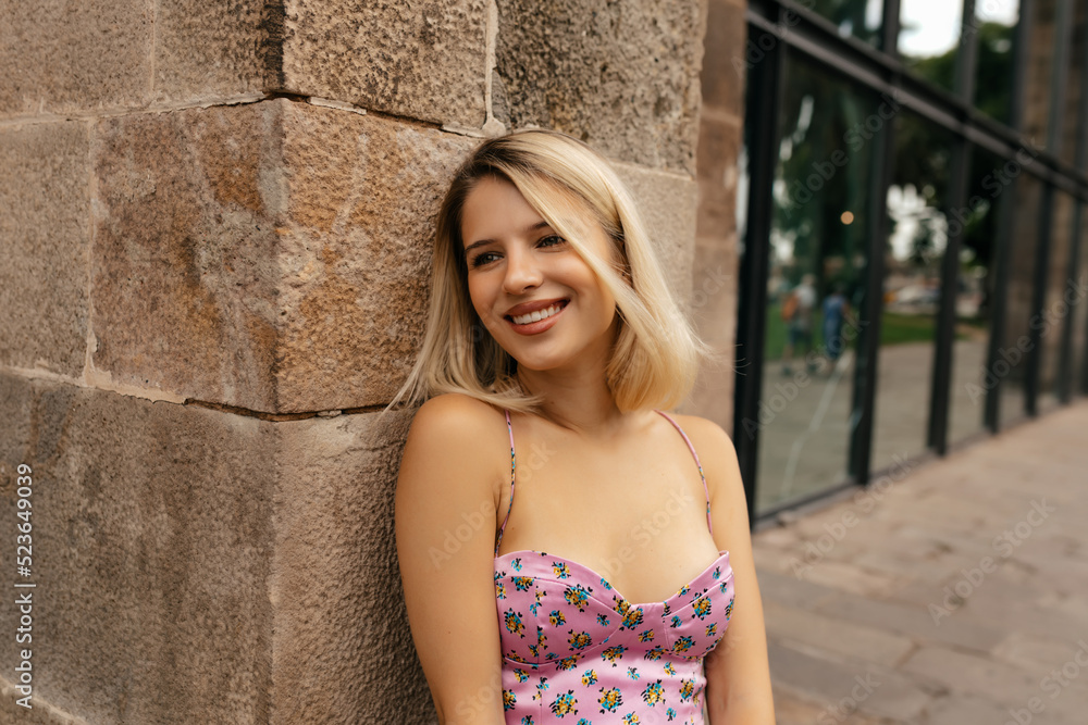 Close up portrait of smiling lovely woman with wonderful smile and short blond hairstyle wearing silk t-shirt with floral print smiling and looking aside. Lifestyle concept