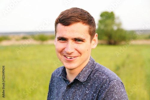 Defocus portrait young man on nature summer background. Smiling young man. 20s years. Handsome man outdoors portrait. Walking in park. Lifestyle. Student. Out of focus photo
